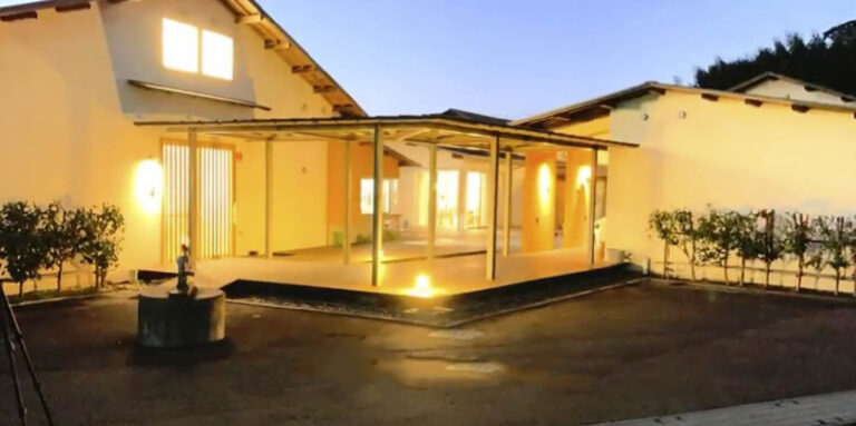 夕暮れ時の介護施設の建物外観。テラス・ウッドデッキと照明が整備された外構。